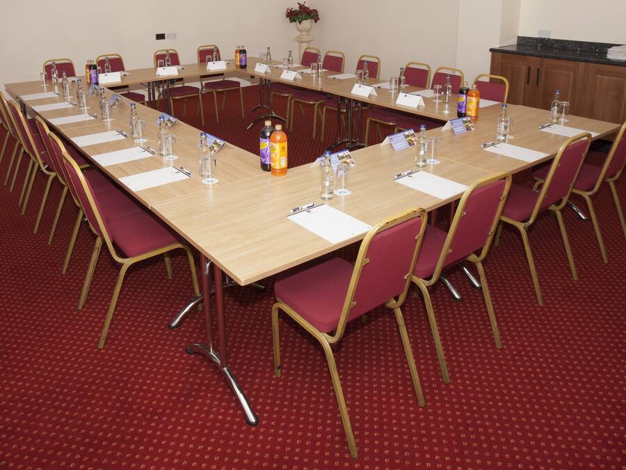 Un salón de conferencias con una larga mesa, alfombra roja y sillas.