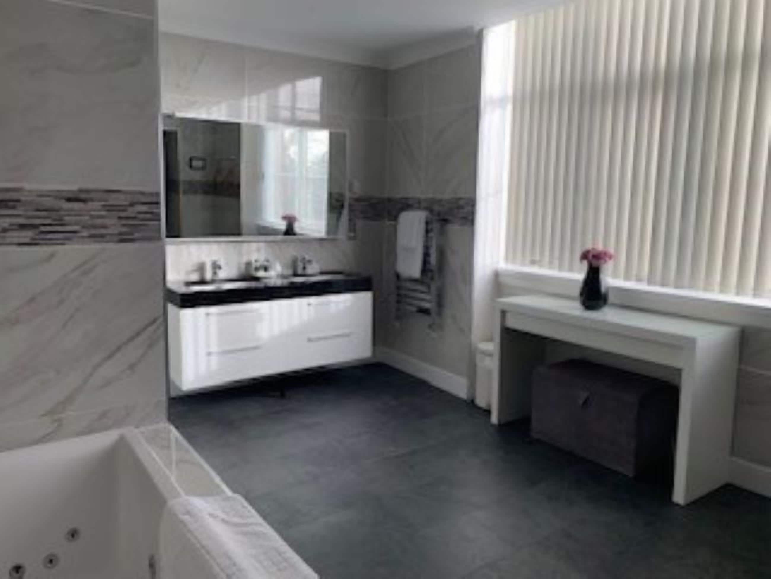 A modern bathroom with a white vanity, a large mirror, and a bathtub.