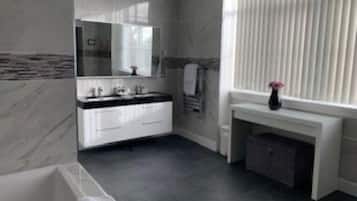 A modern bathroom with a white vanity, a large mirror, and a bathtub.