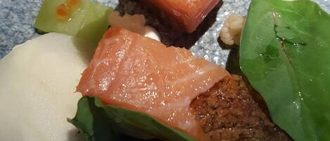 A plate with salmon, greens, and a white spherical item.