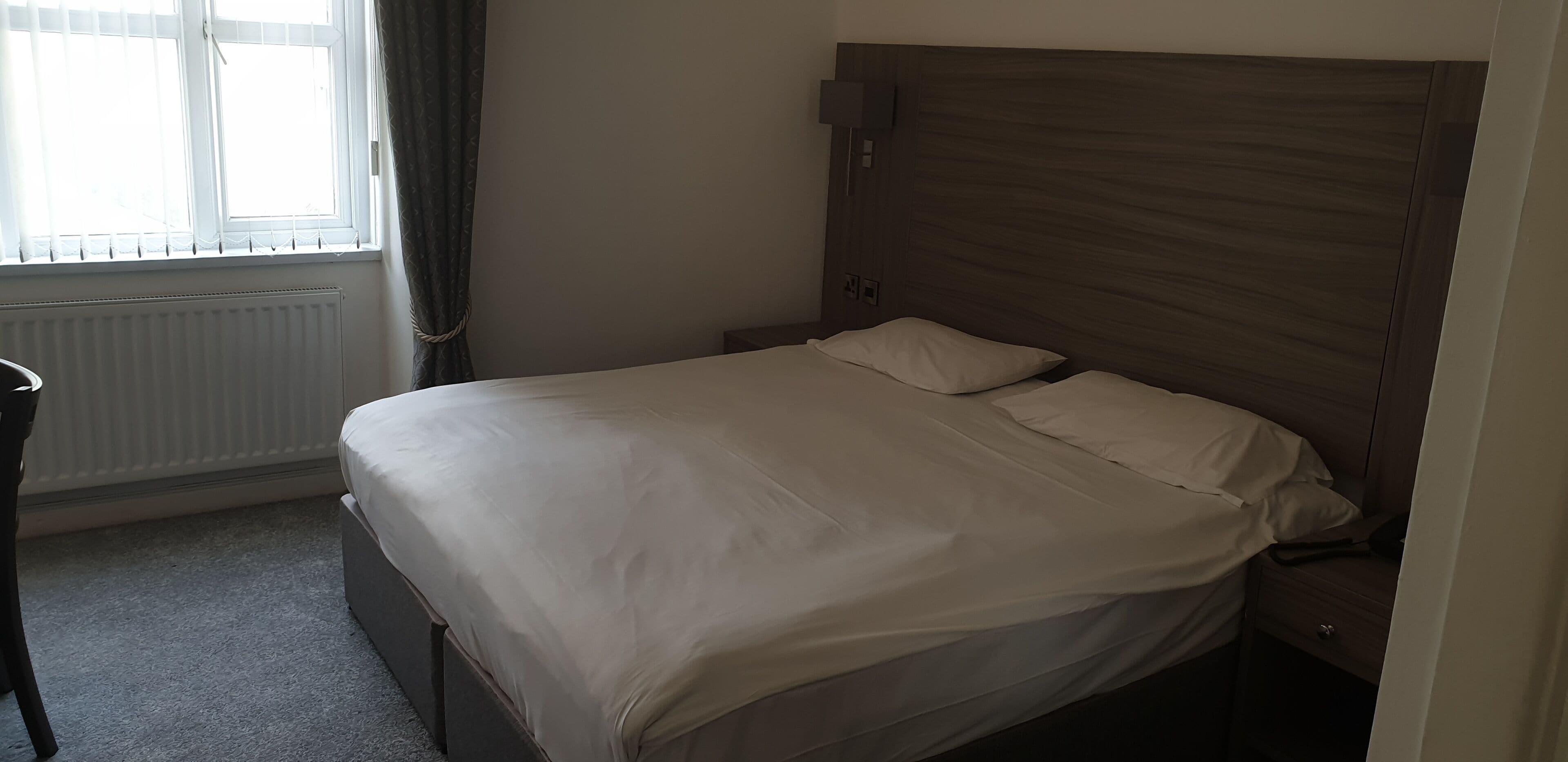 En snyggt bäddad säng med en sänggavel i trä i ett hotellrum.