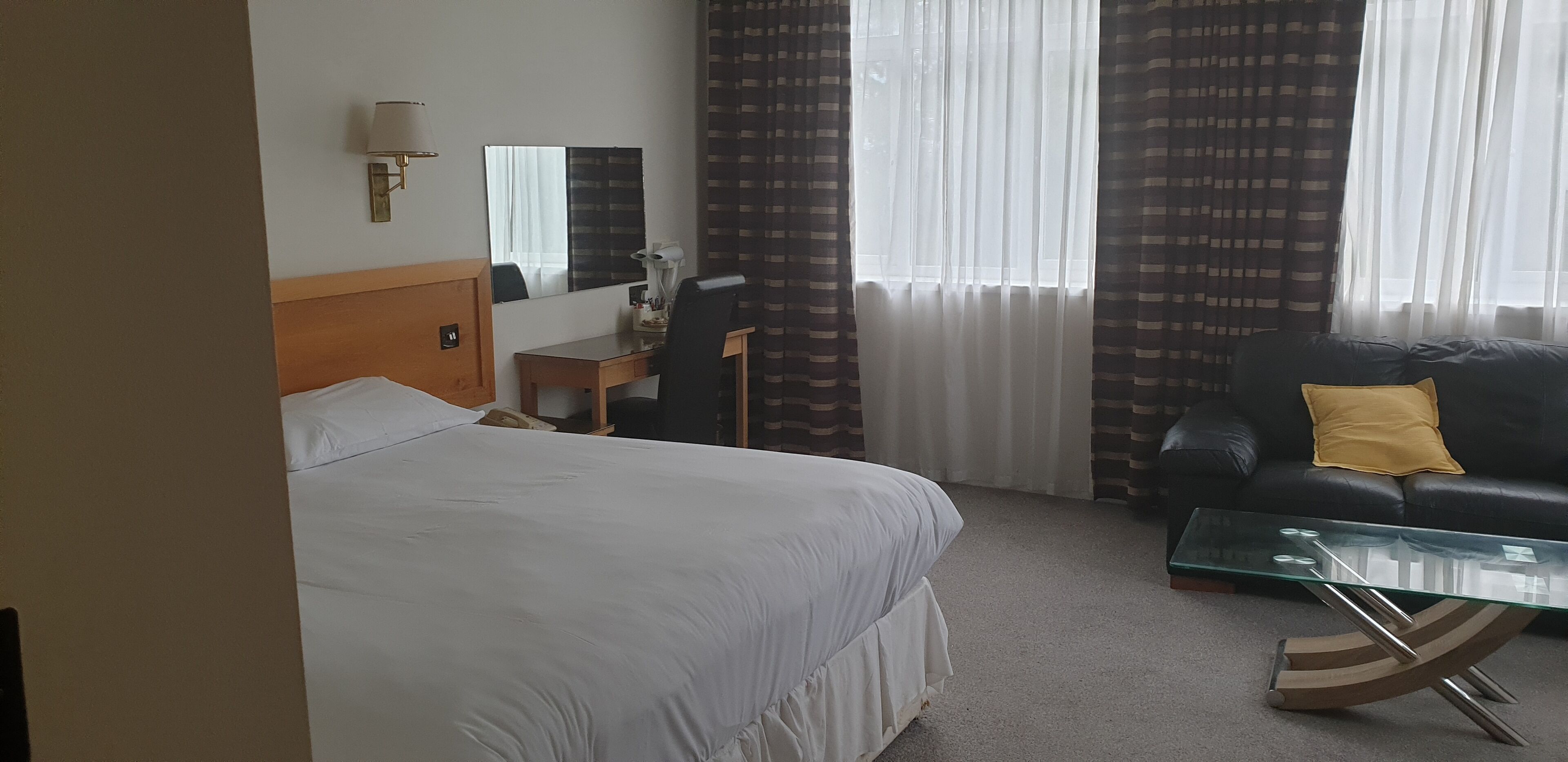 Een hotelkamer met een bed, een bureau, een stoel, een bank en een glazen salontafel.