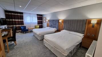 A hotel room with two beds, a desk, a chair, a TV, and a window with curtains.