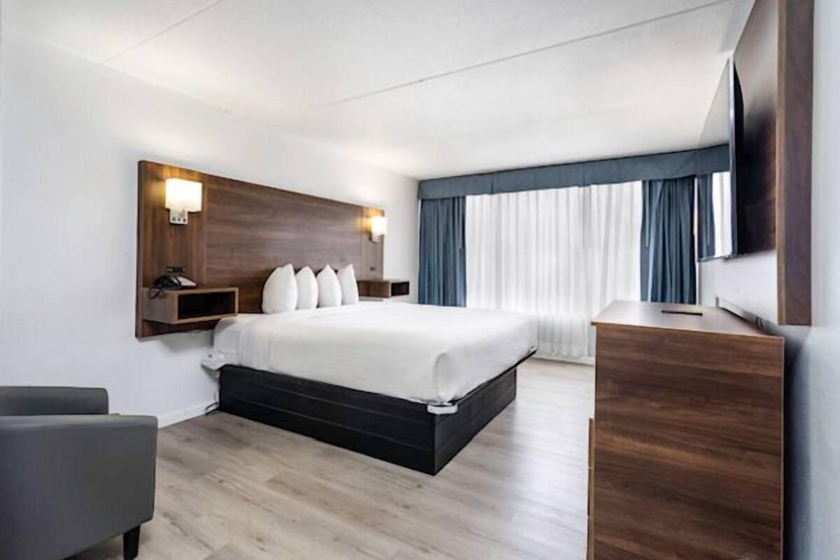 A hotel room with a bed, bedside tables, a desk, a chair, and a TV.