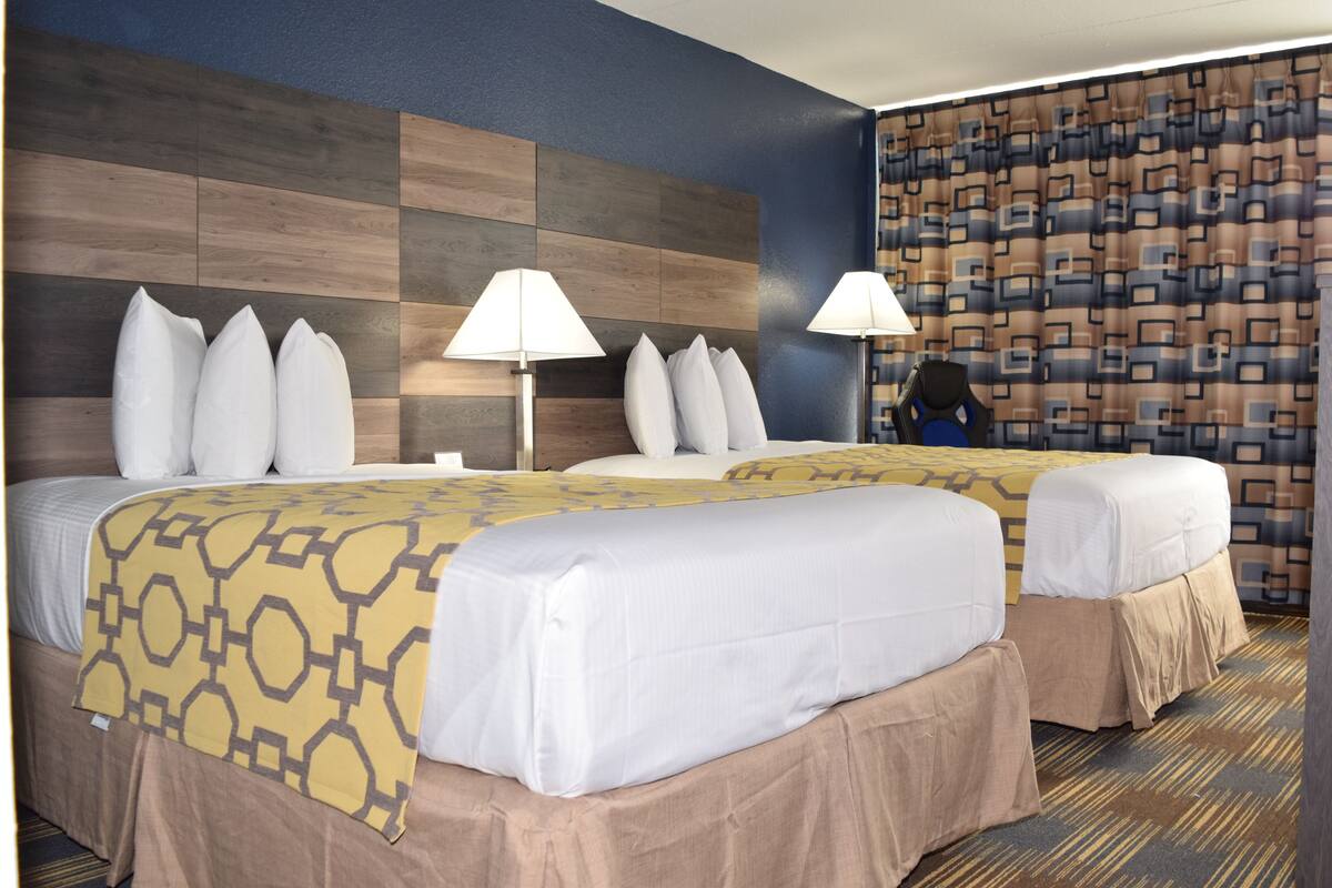 A hotel room with two beds, a large wall unit, and a patterned curtain.