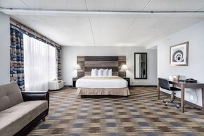 Une chambre d’hôtel avec un lit, un bureau, une chaise, un canapé et une grande fenêtre avec des rideaux.