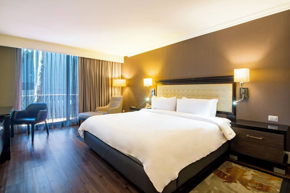 Ein Hotelzimmer mit einem großen Bett, Nachttischlampen, einem Schreibtisch und einem Sessel.