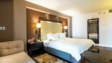 A hotel room with a large bed, bedside lamps, a nightstand, a desk, and a mirror.