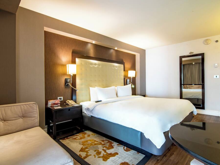 A hotel room with a large bed, bedside lamps, a nightstand, a desk, and a mirror.