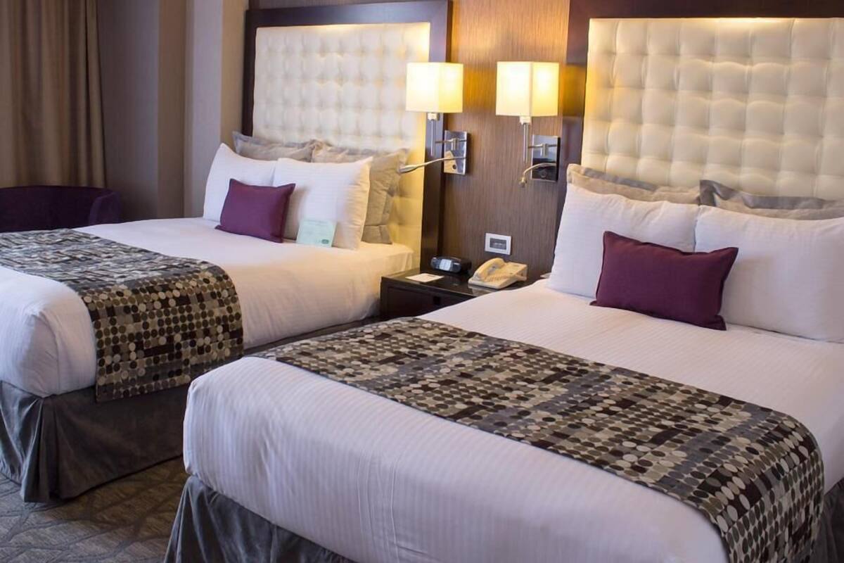 Zwei nebeneinander liegende Hotelbetten mit Kopfteilen, Nachttischlampen und einem Telefon auf dem Nachttisch.