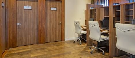 A room with wooden flooring, two wooden doors, and a computer desk with a chair.