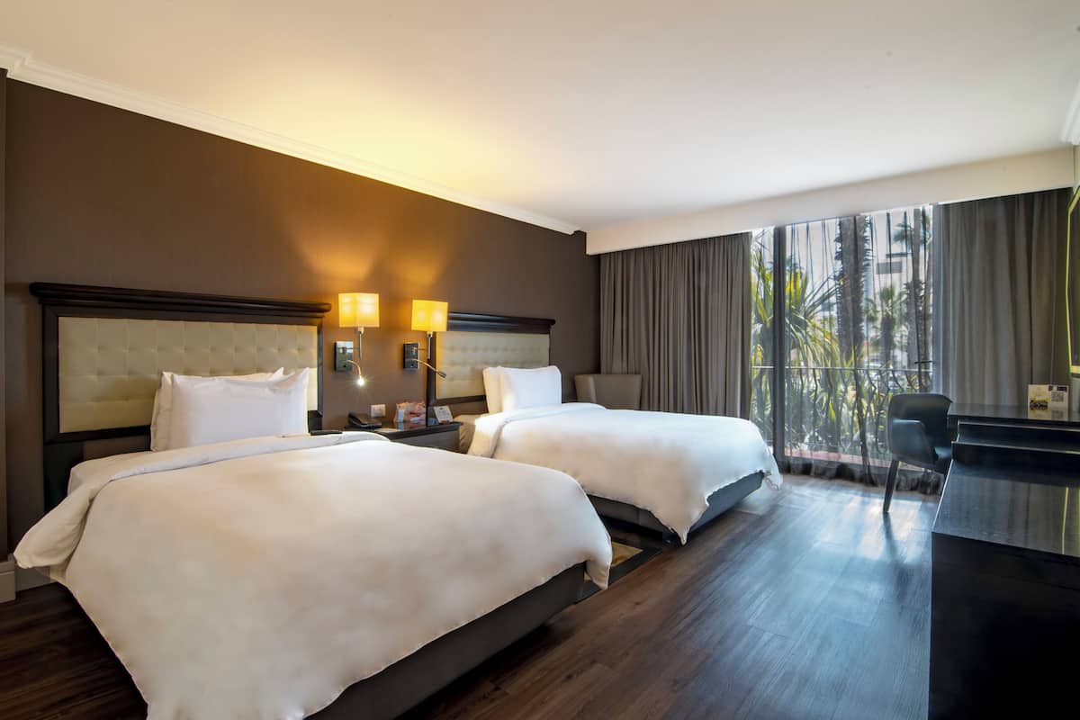 Ein Hotelzimmer mit zwei Betten, einem Schreibtisch und einem großen Fenster mit Vorhängen.