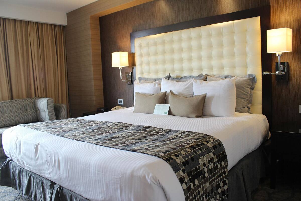 Ein Hotelzimmer mit einem großen Bett, einem Kopfteil, zwei Nachttischlampen, einem Nachttisch und einem Sessel.