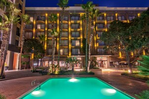 Un hotel con piscina, palmeras y balcones iluminados.