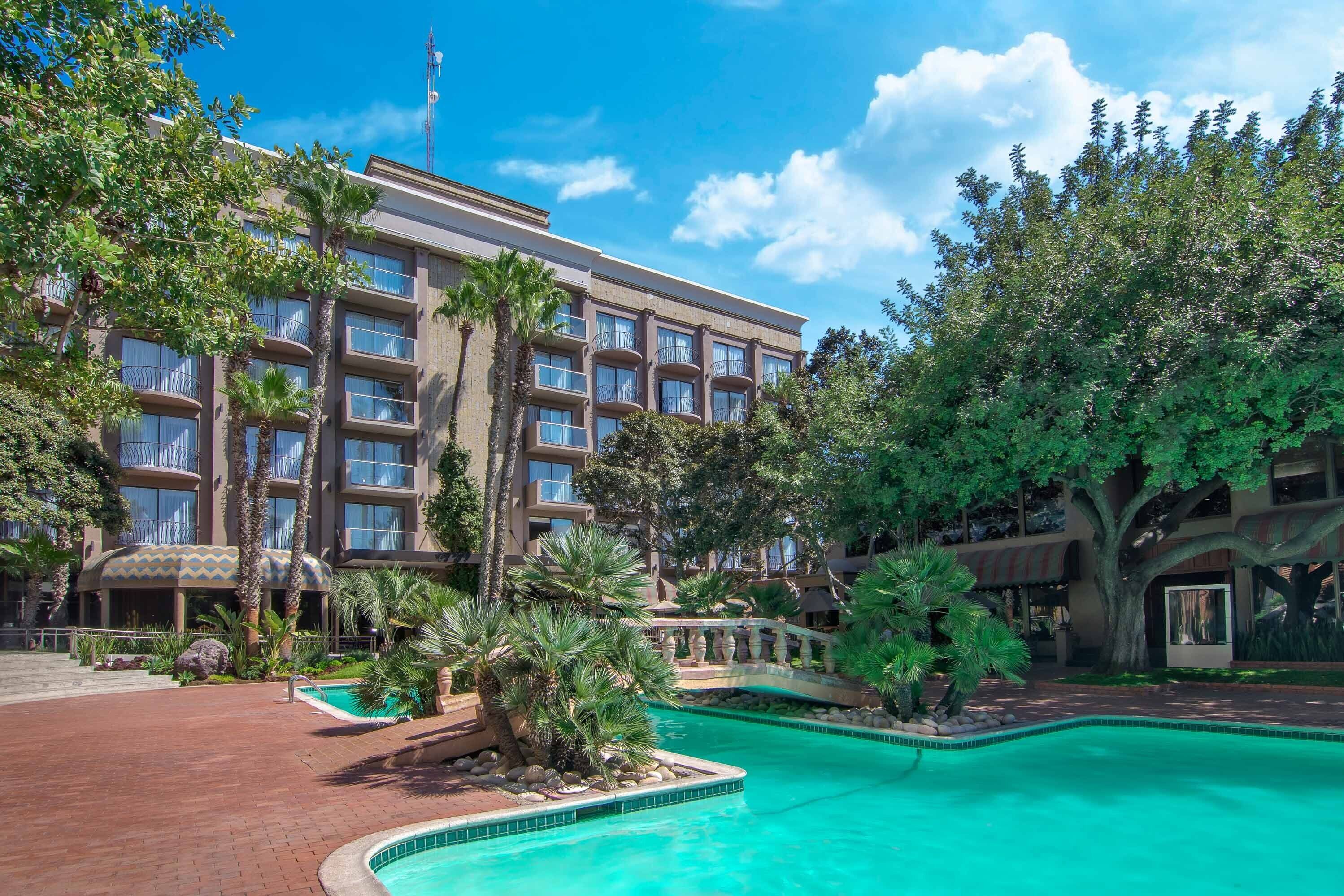 Un hotel con piscina, palmeras y un edificio grande con balcones.