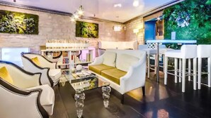 A modern living room with a sofa, armchairs, and a coffee table. There is a bookshelf and a bar area with stools. - Hôtel Eiffel Trocadéro (Paris)