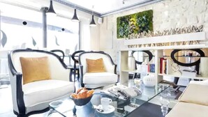 A modern living room with two white sofas with brown cushions, a glass coffee table, and a bookshelf with various items. - Hôtel Eiffel Trocadéro (Paris)