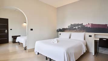 A hotel room with a large bed, a desk, and a chair. There is a painting on the wall and a door leading to another room.