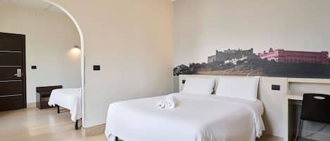 Habitación de hotel con una cama grande, un escritorio y una silla. Hay un cuadro en la pared y una puerta que da a otra habitación.