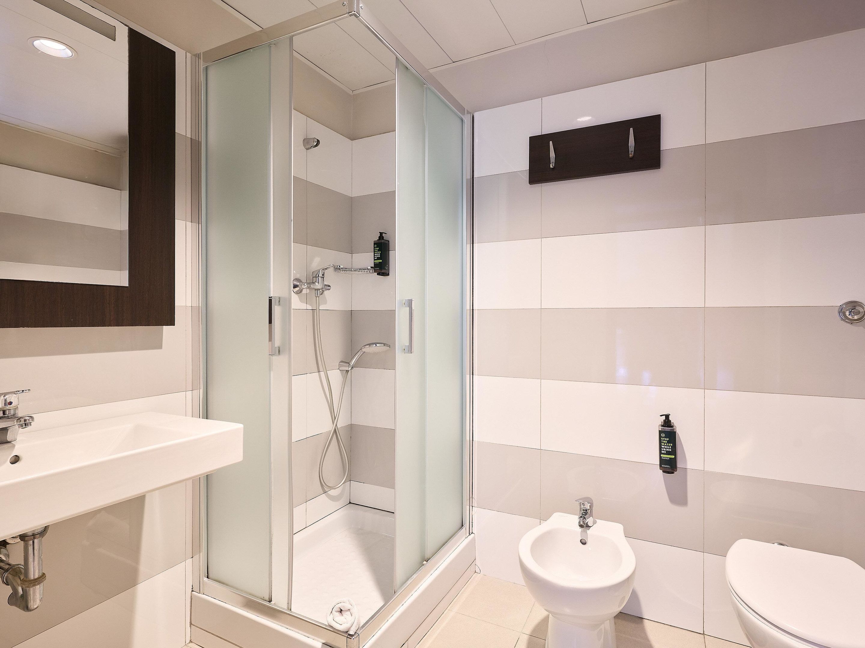 Un baño moderno con ducha de vidrio, un lavamanos blanco y un bidé.