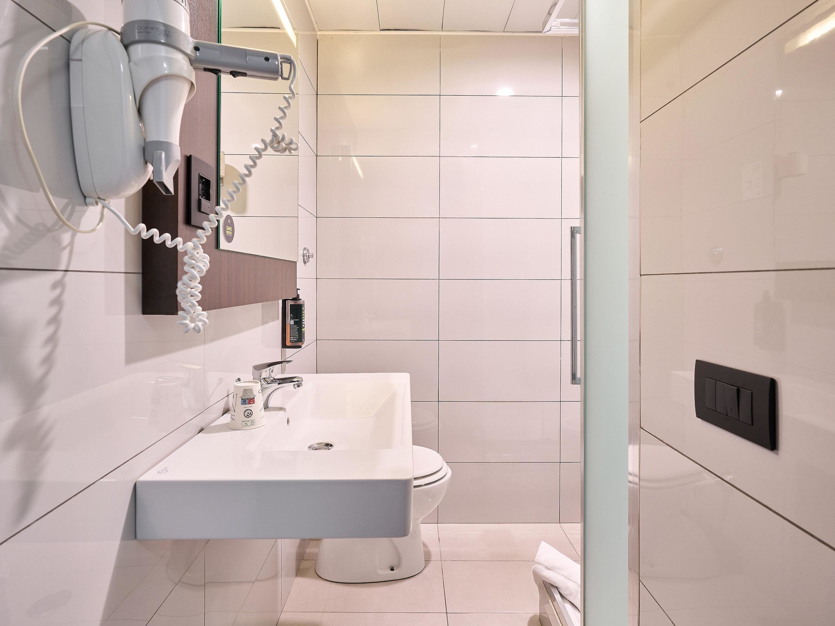 A modern bathroom with a white sink, toilet, and a hairdryer mounted on the wall.