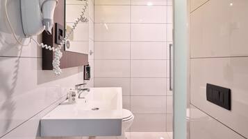 Een moderne badkamer met een wit wastafel, toilet en een haardroger bevestigd aan de muur.
