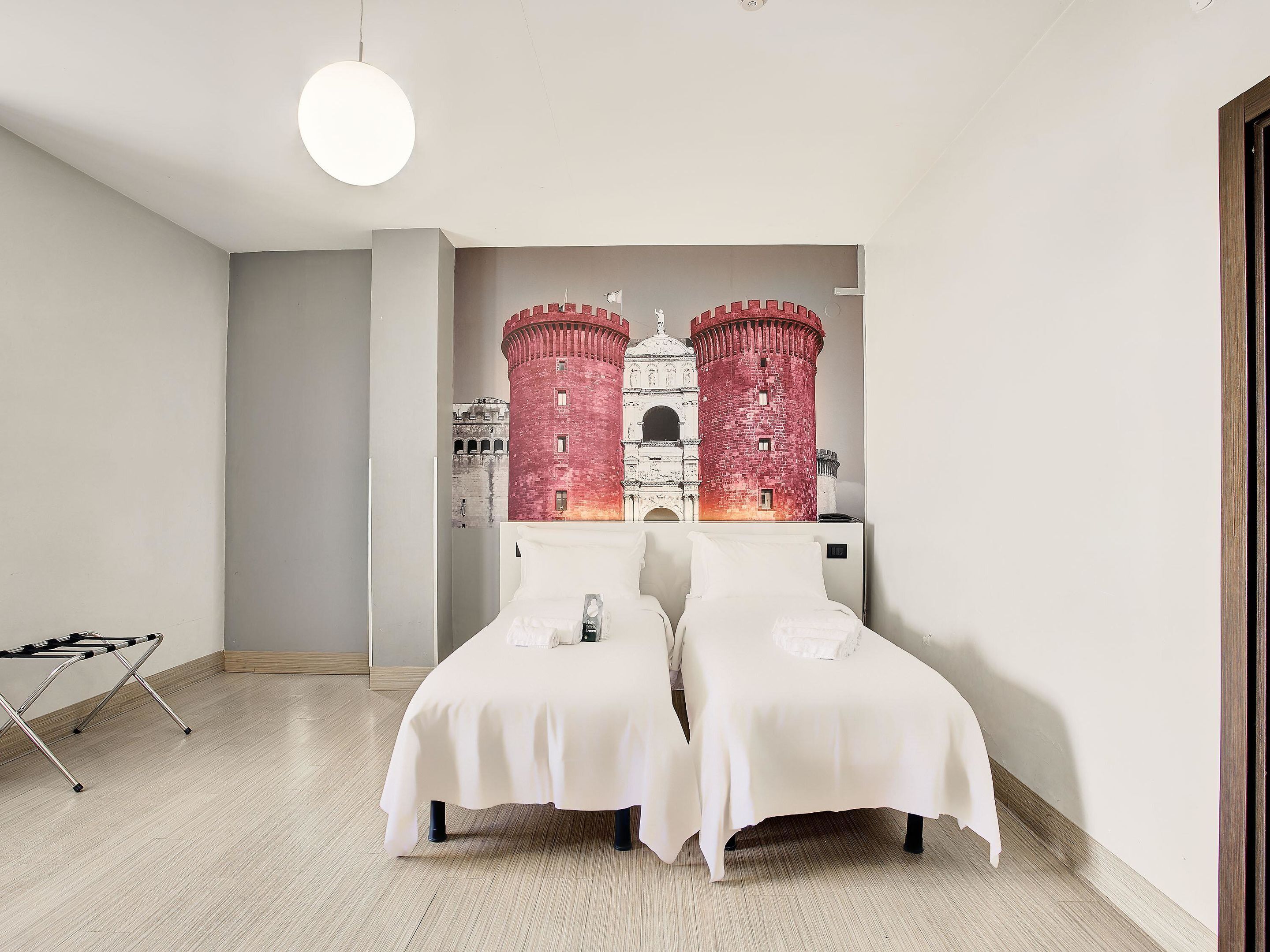 Habitación de hotel con dos camas, un gran mural en la pared con un castillo y una lámpara colgante.