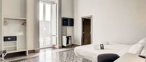 A hotel room with a bed, a desk, a TV, a wardrobe, and a patterned floor.