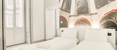 A hotel room with two beds, a large window, and a mural of architectural arches.