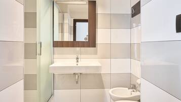 A modern bathroom with a white sink, a mirror, a bidet, and a toilet.