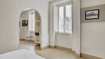 Een hotelkamer met een bed, een garderobe, een kapstok en een raam met uitzicht op gebouwen.