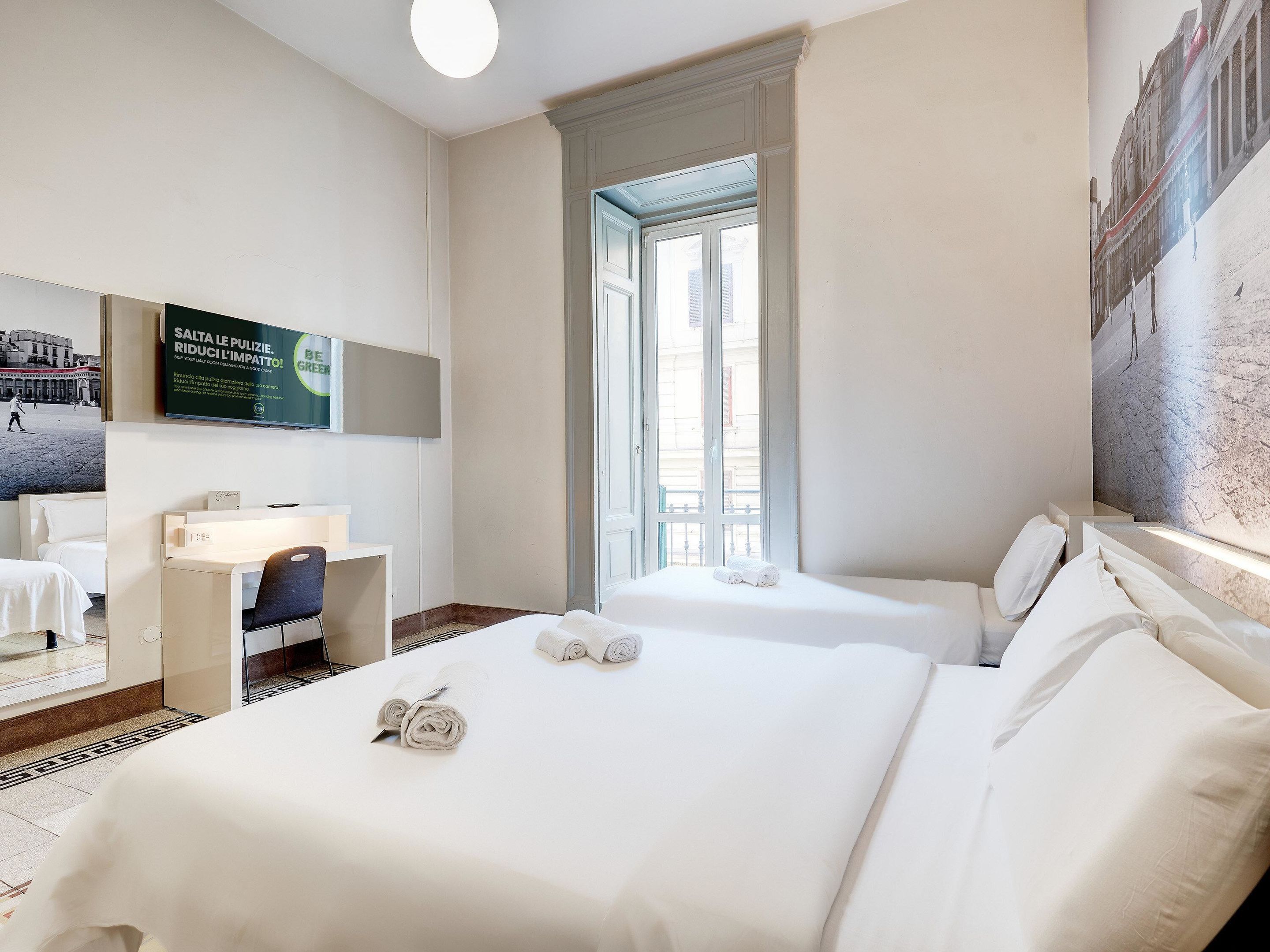 Habitación de hotel con dos camas, un escritorio, una silla y un ventanal grande.