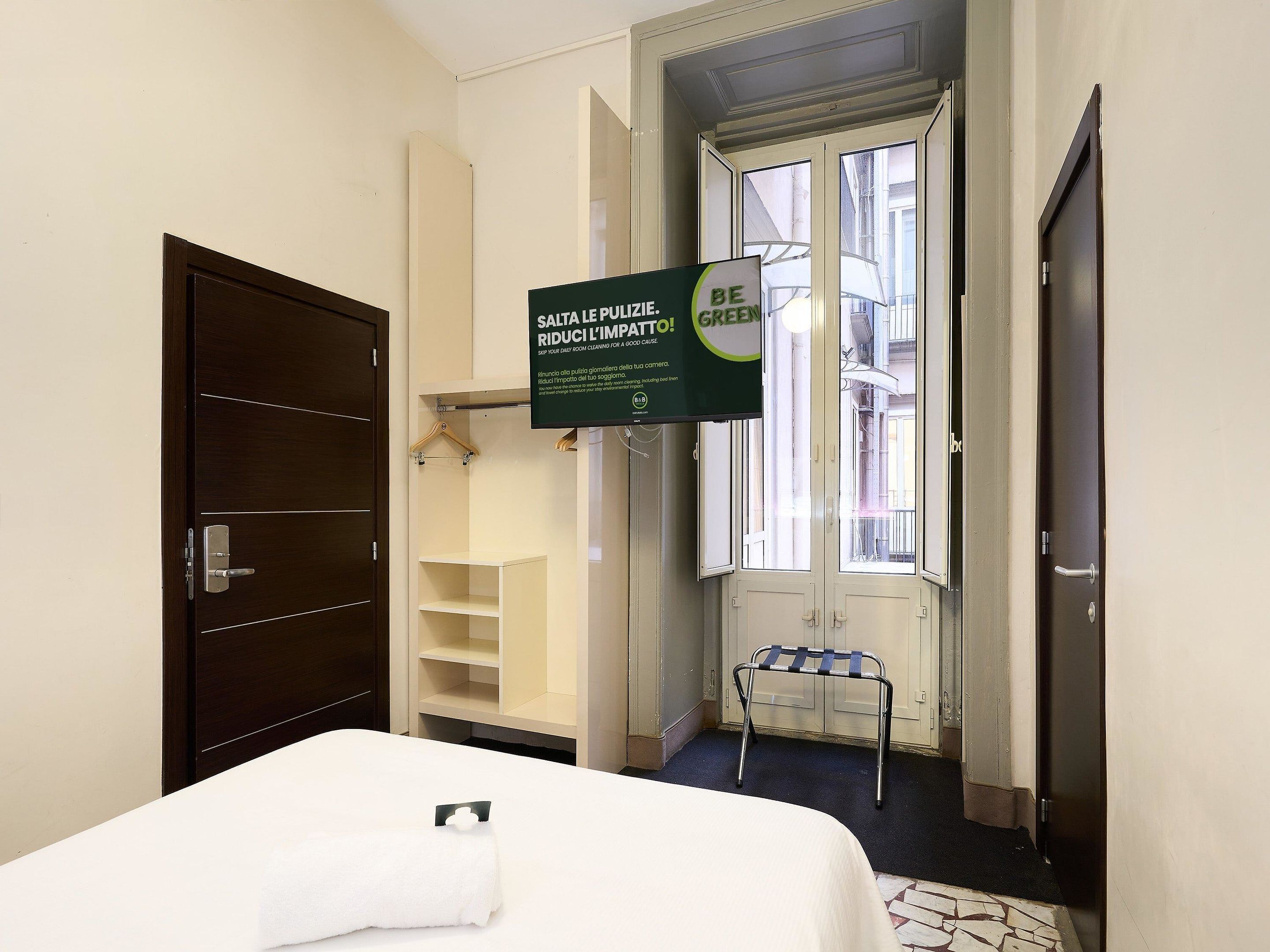 A hotel room with a bed, a hanging sign, a window, and a door.
