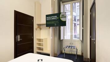 Una habitación de hotel con una cama, un cartel colgado, una ventana y una puerta.