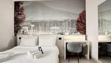Une chambre d’hôtel avec un lit, un bureau et une chaise. La vue donne sur une marina et, au loin, sur une montagne.
