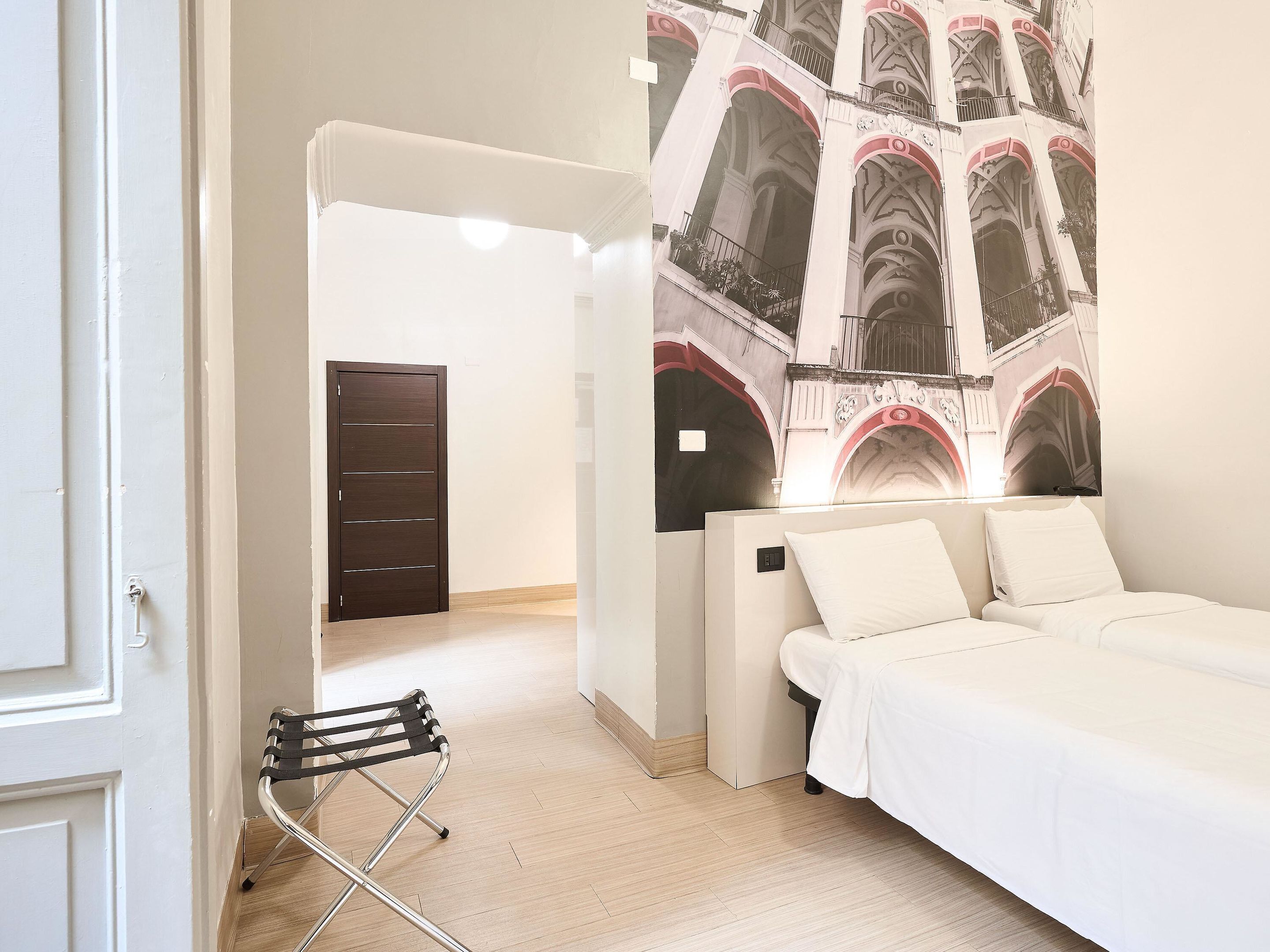 A bedroom with a bed, a chair, a wardrobe, and a wall with a mural.