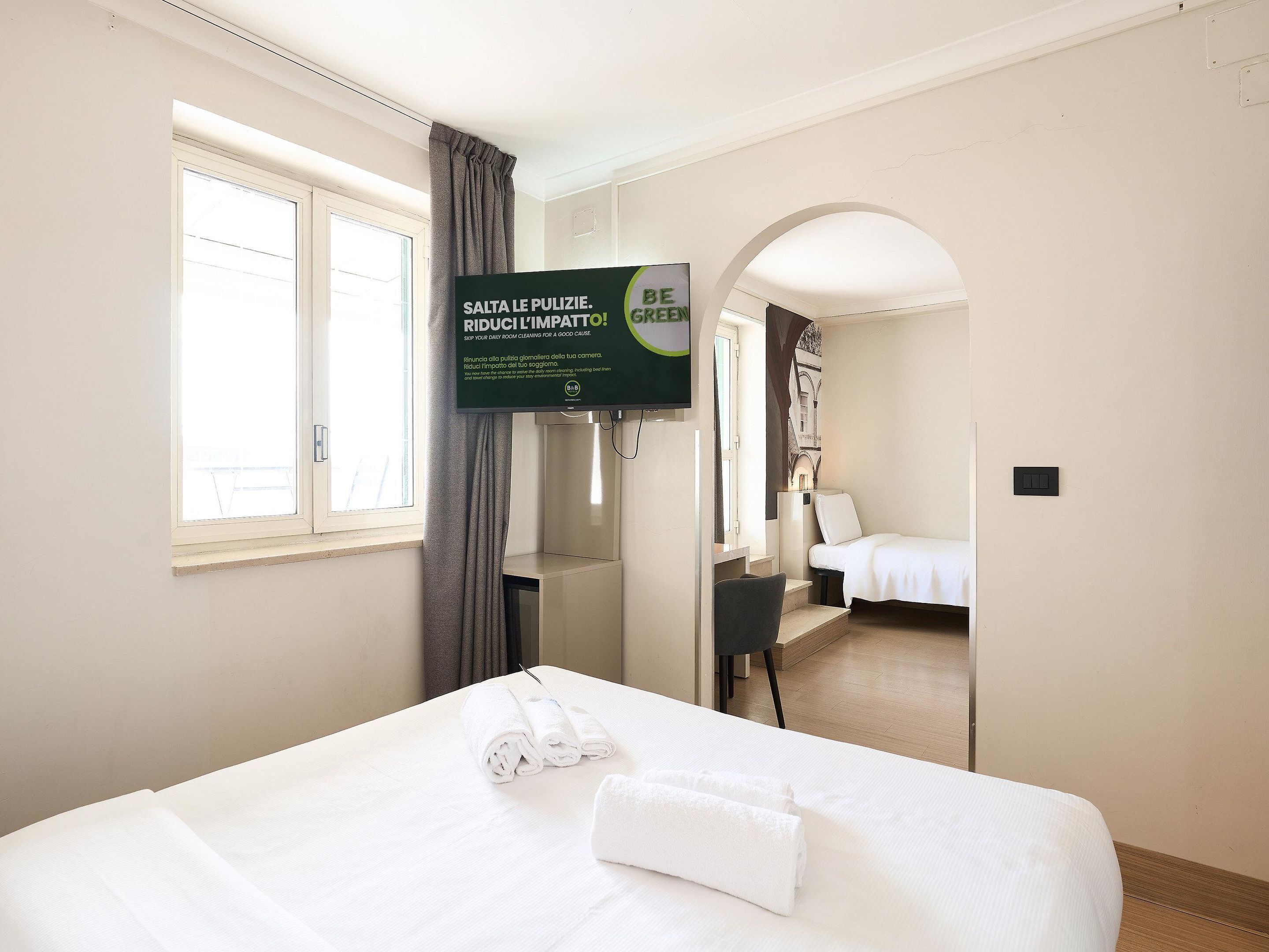 A hotel room with a bed, a TV mounted on the wall, and a window with curtains.