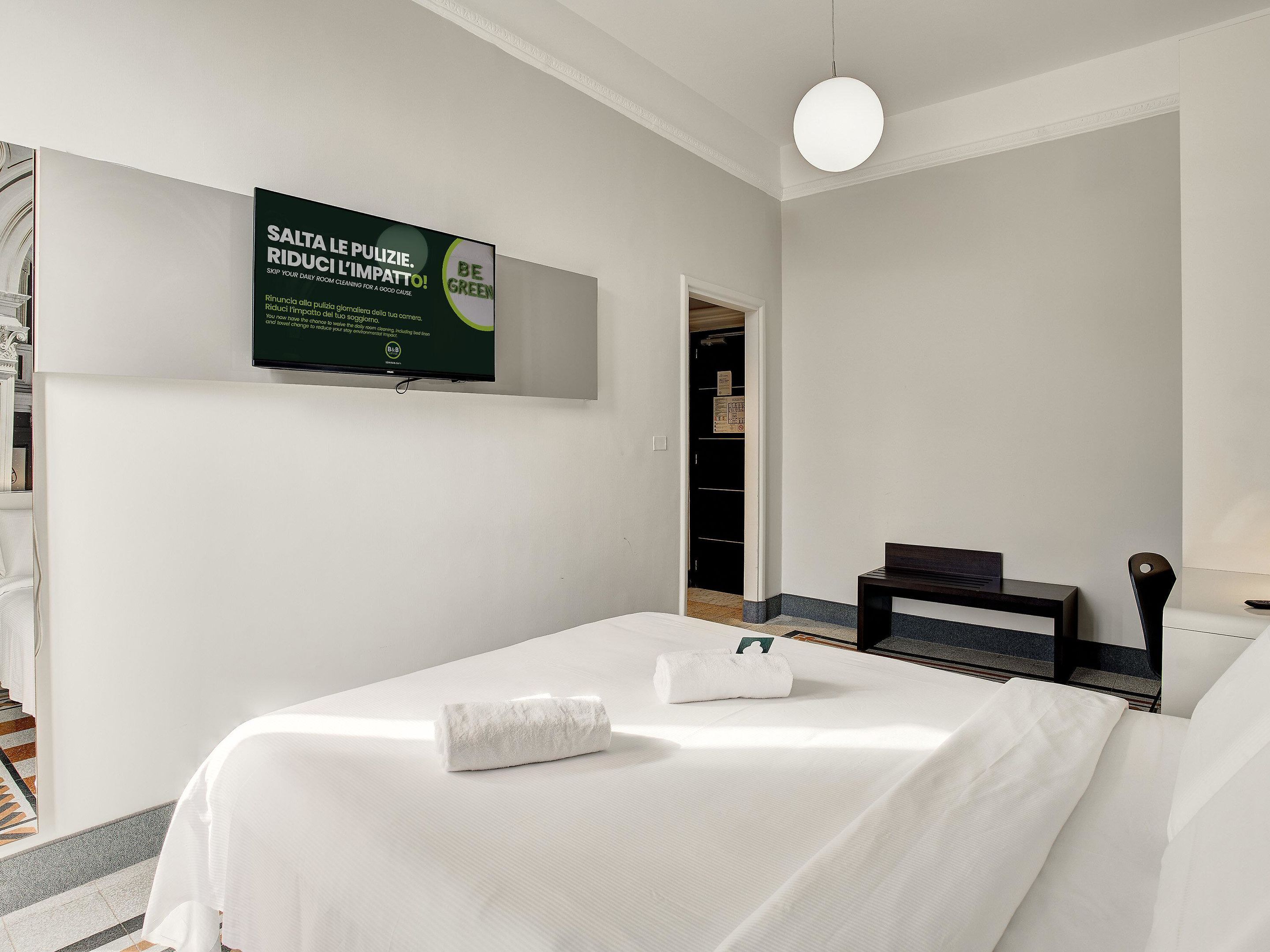 A hotel room with a bed, a desk, and a TV mounted on the wall.