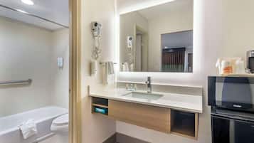 A modern bathroom with a bathtub, toilet, vanity with a sink, mirror, and a hairdryer mounted on the wall.