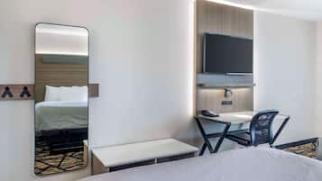 A hotel room with a bed, a desk, a chair, a mirror, a television, and a small table.