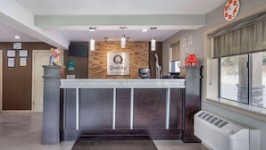 A hotel reception desk with a 'Quality by Choice Hotels' sign, a clock, and a window with blinds. - Quality Inn & Suites Athens University Area (Athens)