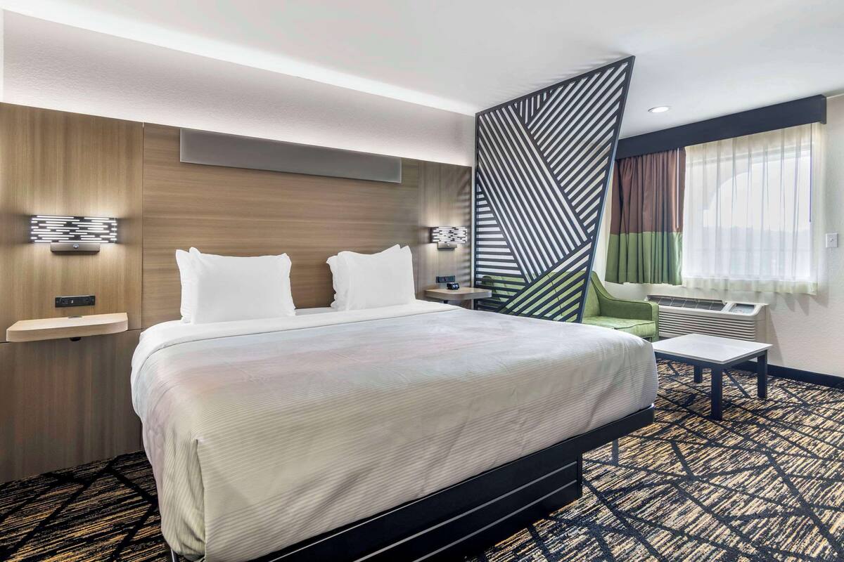 A hotel room with a large bed, a desk, a chair, and a decorative partition.