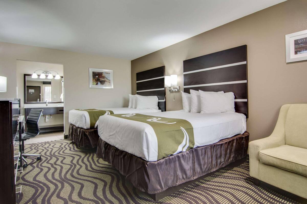 A hotel room with a large bed, two bedside tables, a chair, a desk, a mirror, and a patterned carpet.
