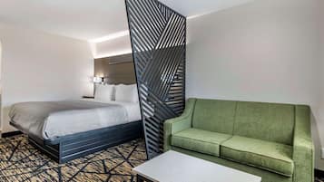 A hotel room with a bed, a green sofa, a small table, and a decorative partition.