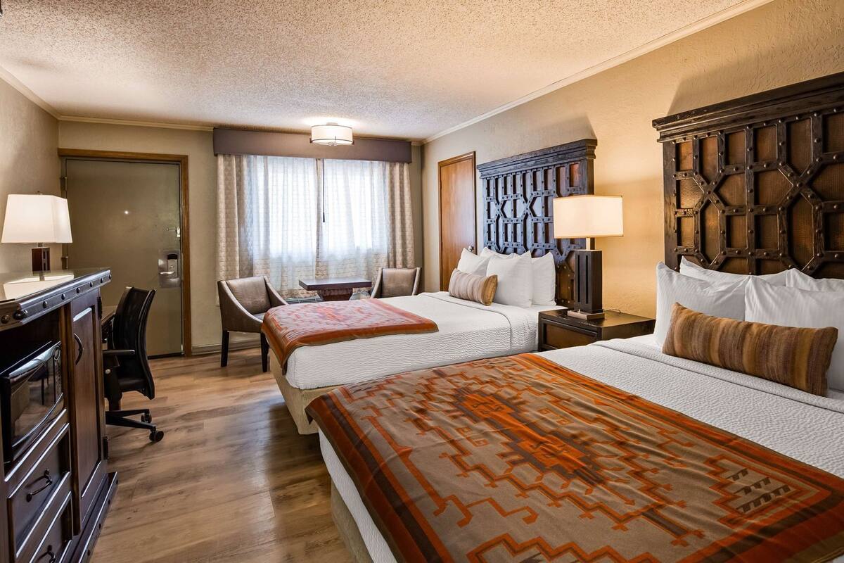 A hotel room with two beds, a desk, chairs, and a small table.