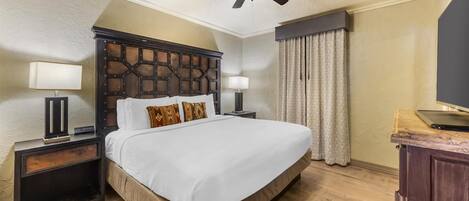 A hotel room with a large bed, two bedside tables with lamps, a ceiling fan, and a wooden dresser.