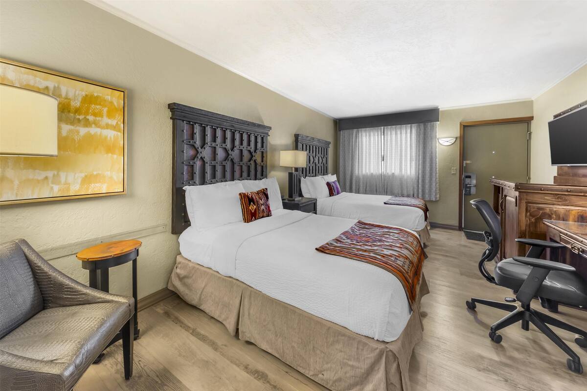 A hotel room with two beds, a desk, a chair, a television, and a painting on the wall.