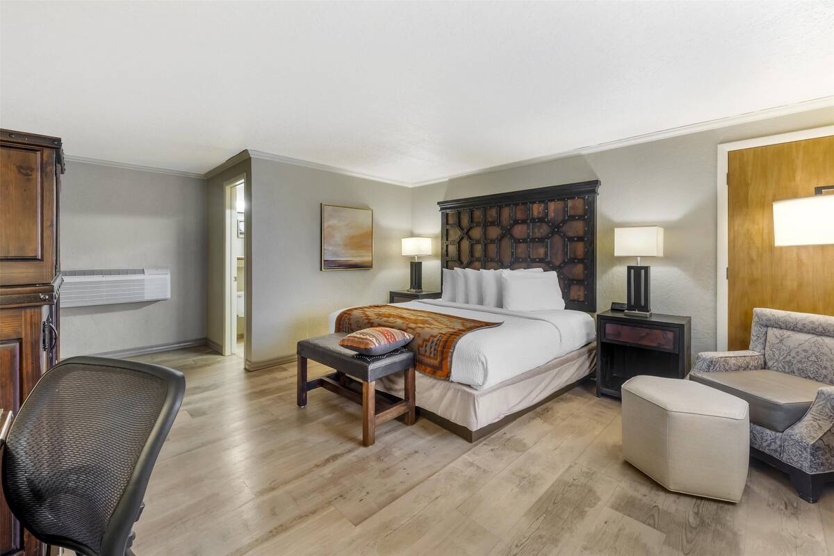 A hotel room with a bed, bedside tables, a chair, a desk, and a lamp.