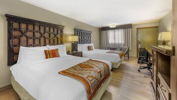 A hotel room with two beds, a desk, a chair, and a mirror.