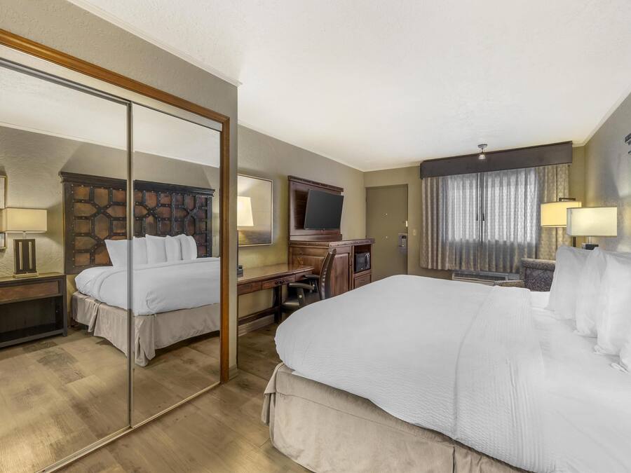 A hotel room with a large bed, a desk, a chair, a TV, and a mirror.